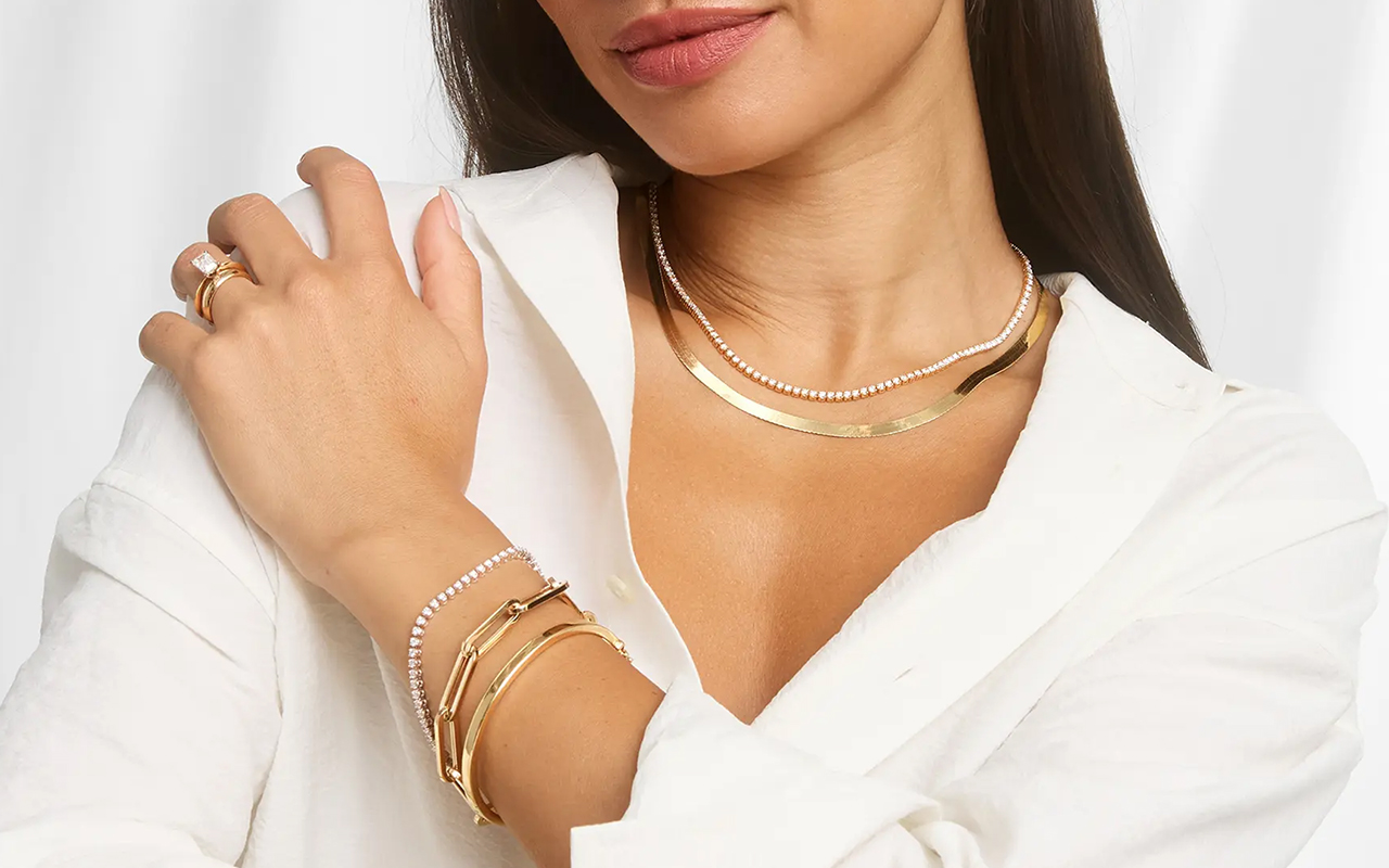 Person wearing jewelry a mix of yellow gold and diamond bracelets, necklaces, and rings against a white background