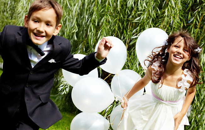 A boy in a suit and a girl in a white dress holding balloons celebrating