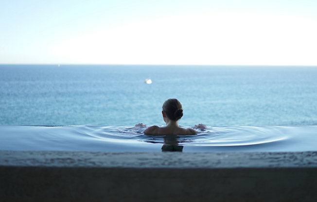 A woman in an infinity pool stares at the horizon