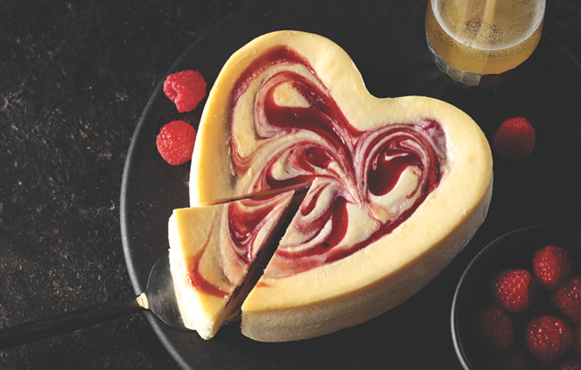 A cheesecake with raspberry swirl in the shape of a heart on a black plate