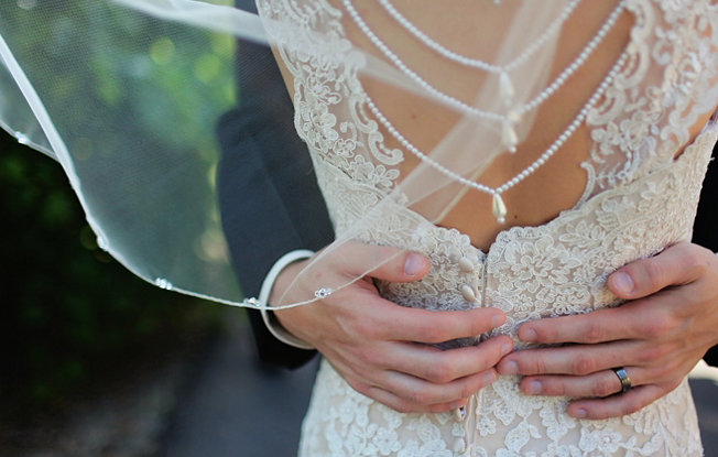 The back of a woman wearing a wedding dress with a man's hand around her waist