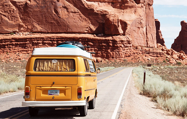 A yellow van drives along an empty mountain road