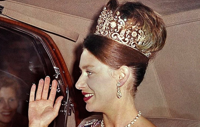 A young Princess Maragret sitting in a car wearing to fans while wearing the Poltimore Tiara