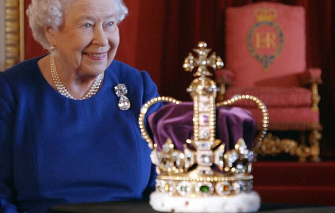 Queen Elizabeth sits smiling at table in front of St Edward's Crown