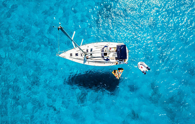 A white boat, pizza shaped floaties and a dingy sit in the middle of clear blue water