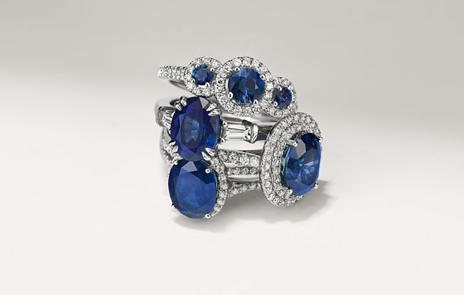four platinum and sapphire rings of various cuts from Blue Nile stacked on top of one another on a white background