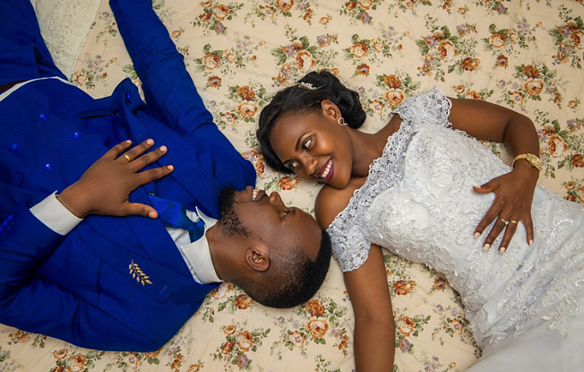 A man in a blue suit and a woman in a wedding dress laying on a floral patterned rug