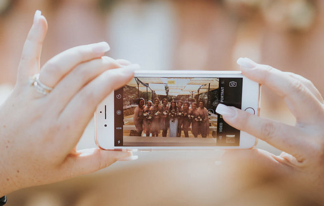 A woman using her smartphone to take a photo of a bridal party