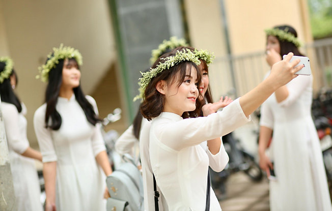 A girl in a white dress and flower crown taking a selfie at a wedding