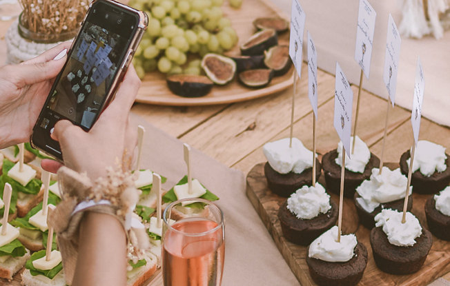 A woman using her smartphone to take a photo of a catering spread at a wedding