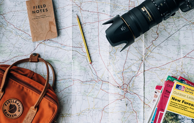 A an orange backpack, travel guidebooks, a camera and a notebook spread out on top of a map