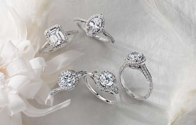 five white gold and diamond engagement rings of various shapes on a white background