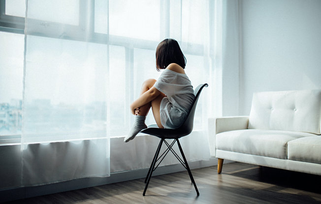 A woman sits on a chair facing a window
