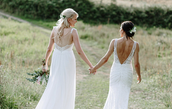 Two woman in wedding dresses holding hands in the grass