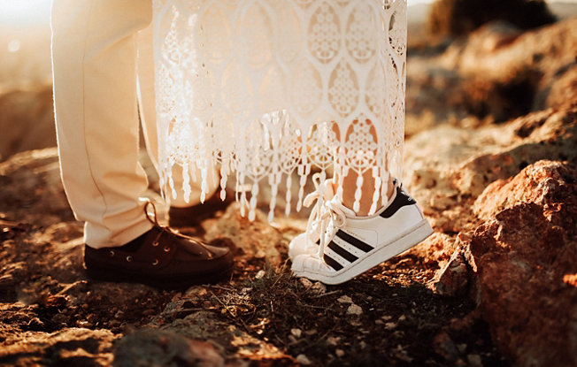 Close up on a couple’s shoes, the bride is wearing sneakers and her wedding dress.