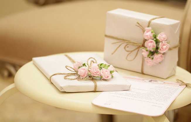 Two gifts wrapped in white paper with flowers on a round table