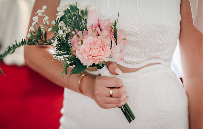 A woman in a two piece wedding dress holding a bouquet of pink flowers